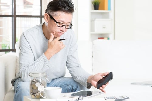 Man seated on a couch evaluating a report on his phone and tablet