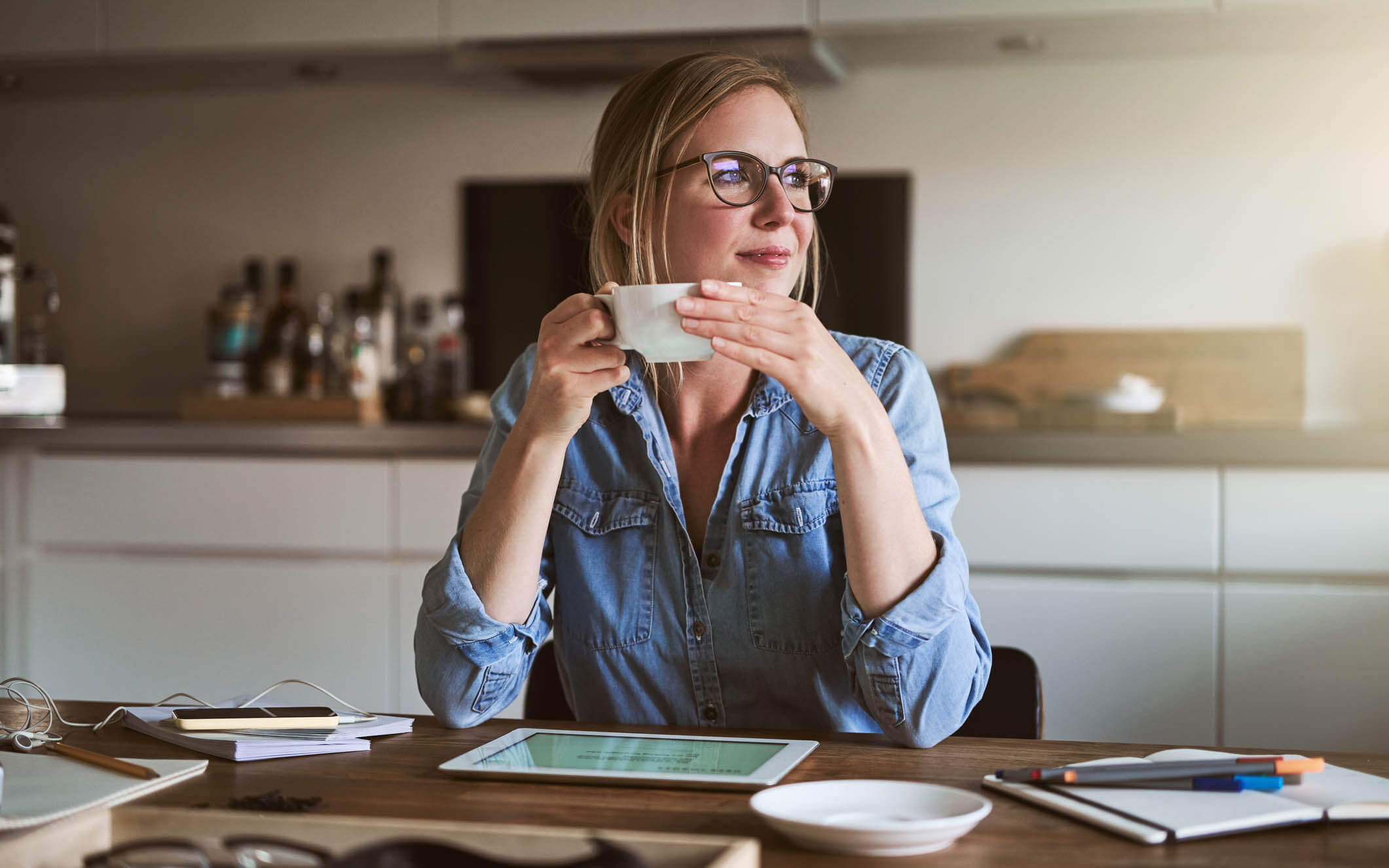 Woman sitting at table drinking coffee and thinking of ways to improve her finances. 