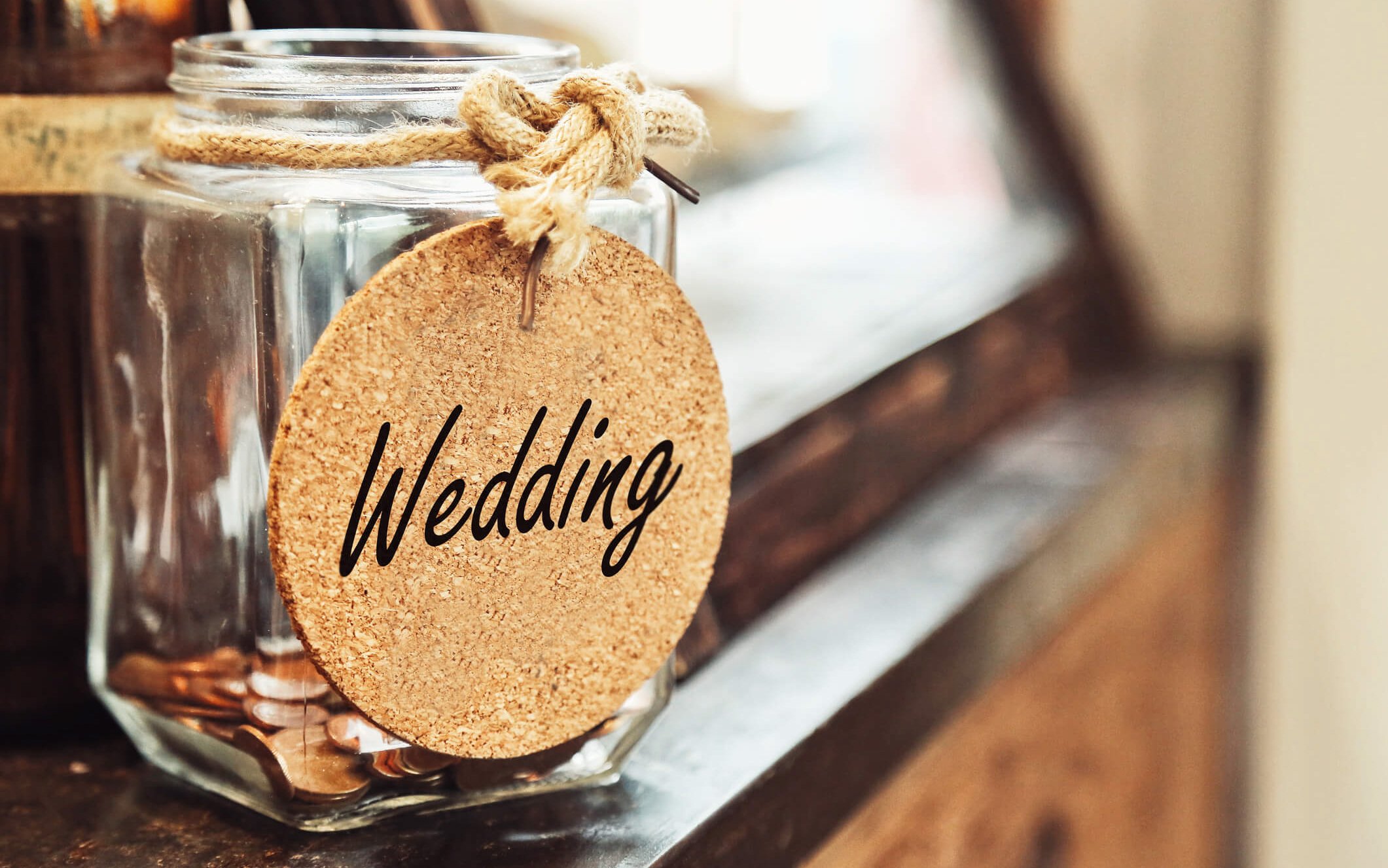 Glass jar full of coins with a cork wedding sign on the front, representing how to plan a wedding on a small budget
