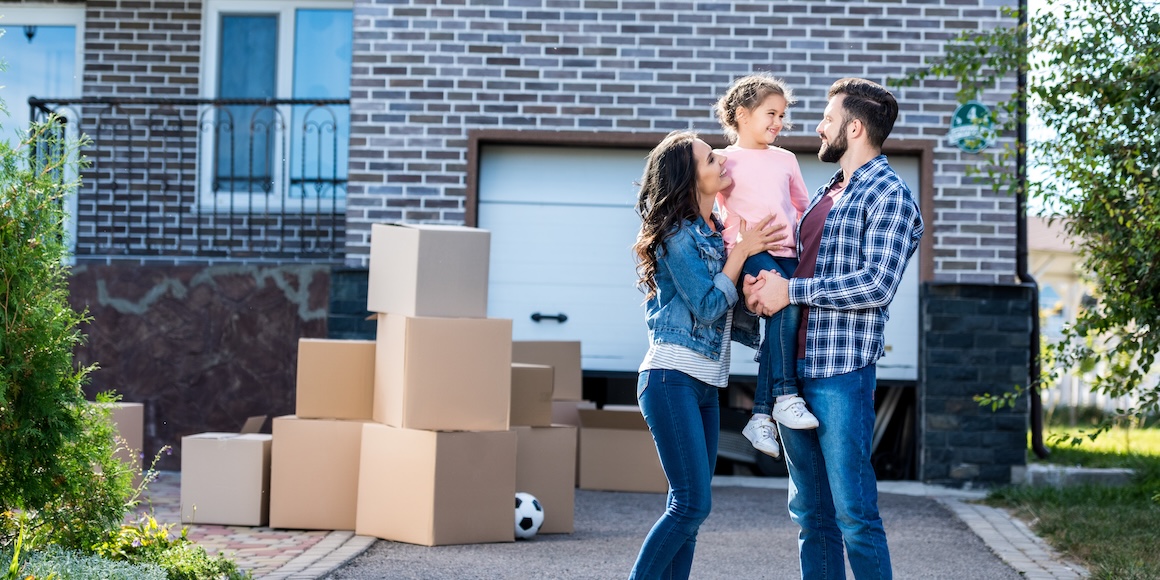First-time home buyers smiling and holding their child in front of their new home in Missouri