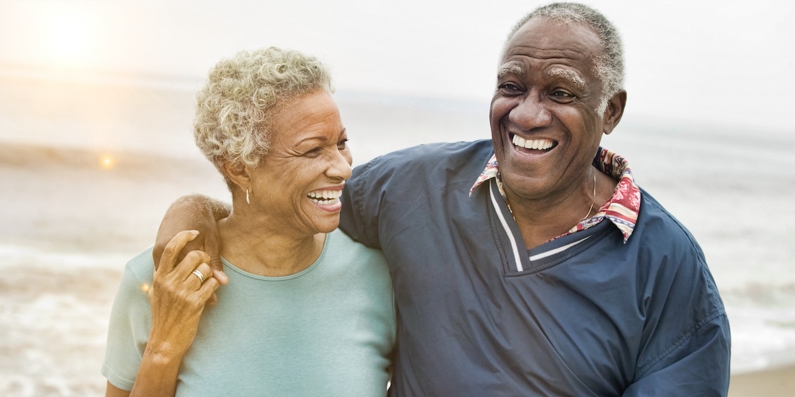 Happy retired couple walking on a beach because they know how much it costs to retire