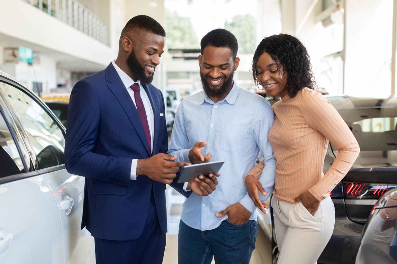Couple talking with a car salesman at a dealership about buying a car