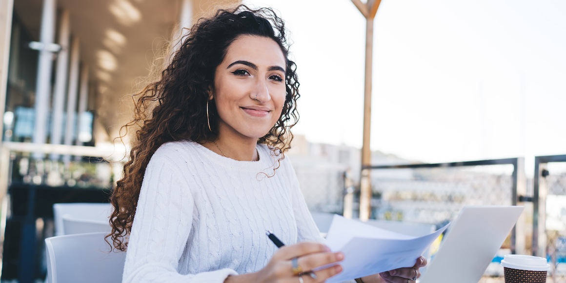 Woman sitting at a laptop, smiling because she’s enjoying the benefits of having good credit