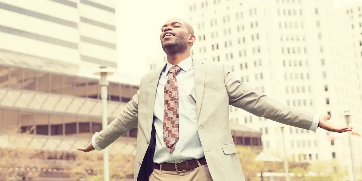 Businessman standing on the street with his arms stretched out and eyes closed because he’s enjoying financial freedom